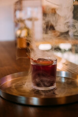 Negroni glass. Smoke drink. Red alcoholic cocktail served with ice cube citrus slice peel. Aromatic refreshing liquor mix on pub counter.