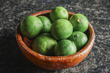 Fresh green limes filling a rustic Clay bowl