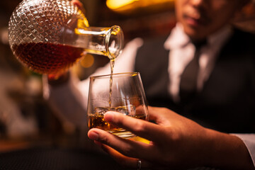 Business man bartender pours whiskey into a glass, sitting sadly in a restaurant.	