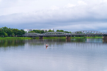 A lone boat glides on the Huong 's River under a cloudy sky, with the historic Truong Tien Bridge in the background, in Hue, Vietnam.