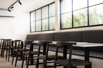 in meeting chairs with tables and sofa arranged in a row near big window and see the green trees outside, on the ceiling have small spotlights
