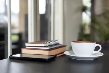 coffee cup with latte coffee and mobile, book for read, diary for taking note on black table