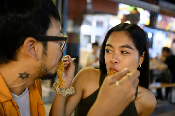 Young asian couple enjoying noodles at night market in southeast asia