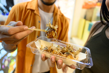 Tourists eating takoyaki in a take away box with chopsticks