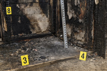Image depicts charred area from fire scene, showcasing evidence markers placed ground. burnt wood and debris suggest investigation into cause of fire, highlighting forensic aspect of arson