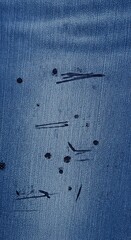 A close-up view of distressed denim, showcasing dark marks and streaks against a light blue backdrop.