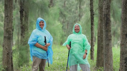 Two elderly Asian women wearing raincoats doing a fun jump pose. Travel, adventure and hiking concept. Retirement lifestyle. Life insurance.