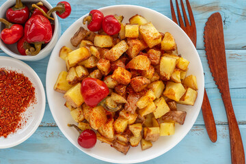 Roasted potato served with mini hot peppers on ceramic plate over blue wooden background. Top view.