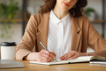 Businesswoman writing down notes on agenda, sitting at office desk, closeup view