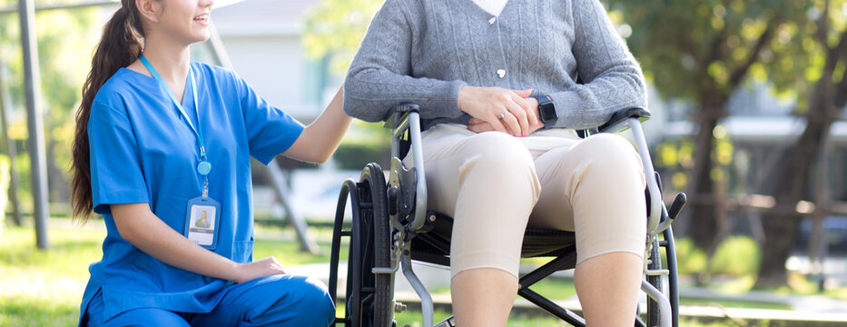 Young caucasian nurse comforting with patient while sitting on wheelchair in outdoor park, doctor woman support and counseling with patient, caregiver and service with senior, medical and consoling.