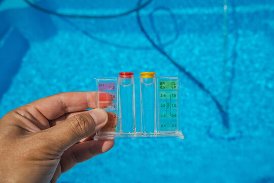 Fototapeta A person holds a clear pool water tester with pH and chlorine indicators above a sparkling blue swimming pool during regular maintenance on a sunny day.