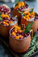Four festive copper mugs filled with a holiday cocktail, garnished with cranberries, orange, rosemary, and cinnamon stick for celebration.
