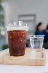 Iced black coffee in a transparent plastic cup on wood tray