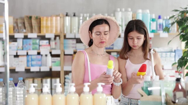 Portrait of interested mother and daughter customers preparing for summer season, holding and examines label and content of mosquito repellent in modern drugstore  - Powered by Adobe