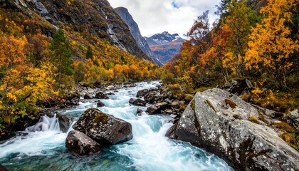 Cascading turquoise river rushes through a deep valley surrounded by autumn trees and towering mountain faces under a cloudy sky