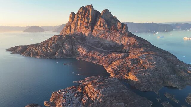 Town Uummannaq during summer in northern West Greenland beyond the Arctic Circle. Greenland, Danish territory. Large mountains and glaciers in the background. Misty morning. Fjord in Greenland. Aerial