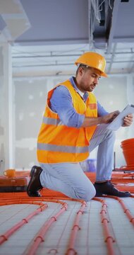 Vertical shot of a construction inspector checking a building site using a digital tablet to control the quality of an underfloor heating installation indoors.