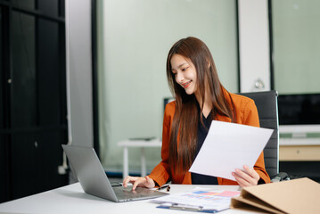 Fototapeta premium Confident businesswoman working on a laptop at a sleek office desk, showcasing professionalism, productivity
