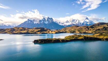 Serene blue lake reflects mountain peaks, framed by rolling hills under a partially cloudy sky in a scenic landscape