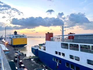 ships were docked at the pier with calm seas and the setting sun creating a serene atmosphere