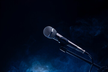 Black and silver microphone in studio, on a concert stage with fog and light coming from behind a black and dark background. Professional recording equipment.