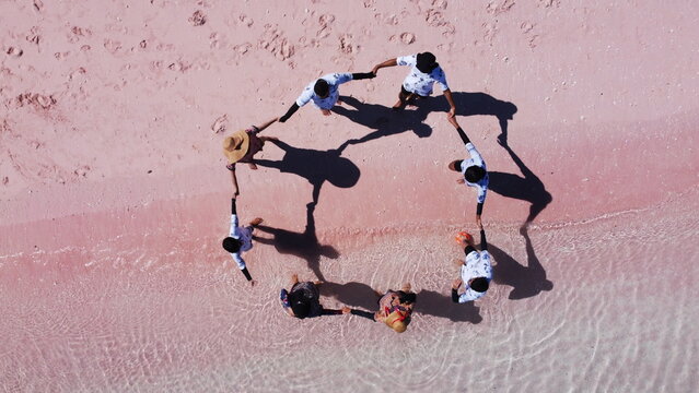 Drone shot of people holding hands in a circle on a stunning pink beach shoreline. Ideal for concepts of friendship, teamwork, unity, and tropical island getaways in Labuan Bajo beach