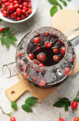 Steaming rosehip tea brewing in glass teapot with fresh rose hips