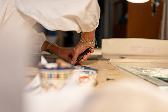 Gros plan sur une femme artisan vitrailliste en train de manipuler des vitraux dans son atelier, montrant pr&eacute;cision et savoir-faire.