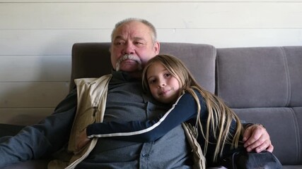 Elderly man seated on a couch, embracing young girl with affection, showcasing a heartwarming moment of connection and love during a family gathering, celebrating the bond across generations
