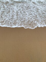 Ocean wave washing sandy beach background with sea foam texture for summer, travel, vacation or nature design