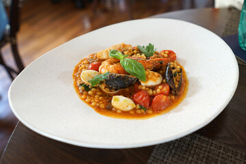 Close up plate of Fregola Pasta with seafood in red sauce- Italian cuisine