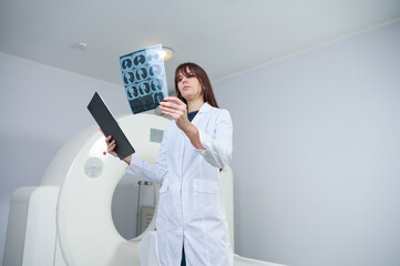 Young female radiologist staying in scanning room holding CT film. Working in the clinic. Pretty...