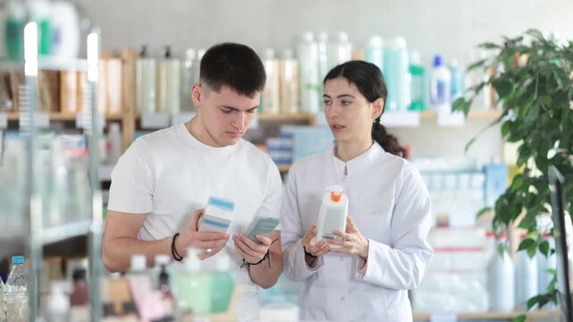 Man chooses skin cream in modern pharmacy. Female pharmacist helps with choosing a medicine. High quality 4k footage