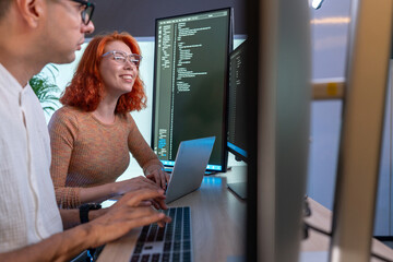 Two developer focus on coding at their desk, surrounded by multiple computer screen displaying line of code in a contemporary workspace, enhancing teamwork and creativity.