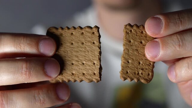 A man holding a chocolate chip cookie.
A guy holding two halves of a cookie in his hand.
A crispy, brittle shortbread cookie.
A chocolate cracker or cookie in his hands.