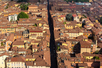 A high-angle aerial view of a narrow, historic Italian street cutting through a dense grid of traditional buildings with red-tiled roofs, perfect for urban planning or travel-related content.