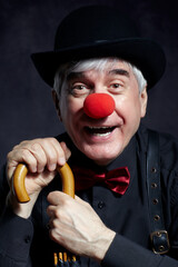 Portrait of laughing  clown against a dark background leaning on the handle of an umbrella.
