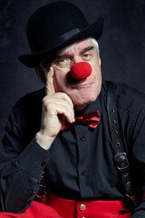 Dramatic portrait of a sad clown against a dark background. Hand near face.