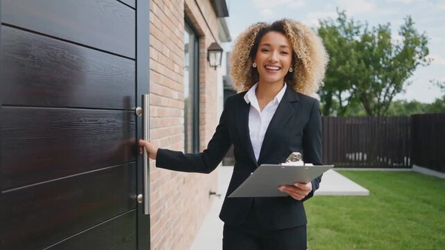 Smiling real estate agent holding clipboard and opening front door of modern brick house. Property showing, home selling and real estate service concept. Design for banner, poster, header. Side view p