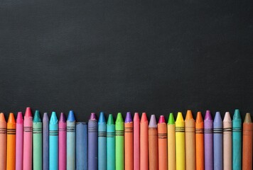 Row of colorful crayons lined up at the bottom edge of a matte, dark, textured background. Copy space above crayons