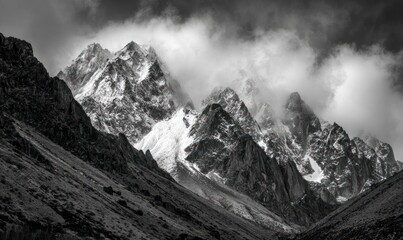 Dramatic monochrome mountain peaks shrouded in clouds, with snowy summits and jagged ridges, captured in stark black and white