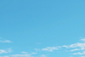 Fototapeta premium A serene vista of a pastel-blue sky dotted with wisps of soft white clouds at the bottom edge, suggesting open space and calmness