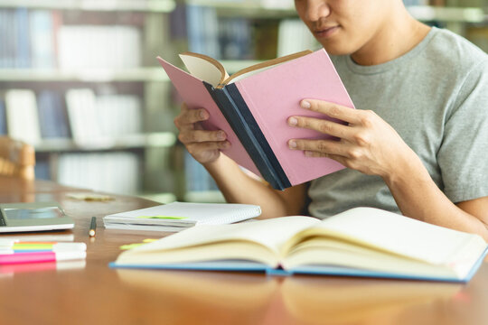 male asian student studying and reading book in library - Powered by Adobe