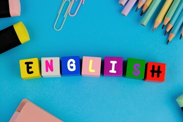 Word LEARN ENGLISH made with carved letters on blue desk with office or school supplies, stationery. Concept of English language courses
