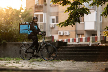 Obraz premium Delivery man riding bicycle in urban setting during sunset