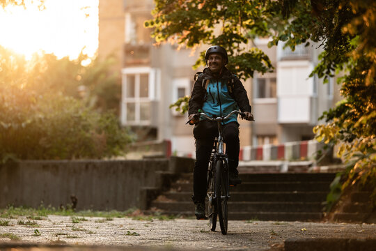 Smiling delivery woman riding bicycle at sunset in the city