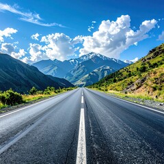 Fototapeta premium Scenic highway stretching towards snow-capped mountains beneath a cloudy blue sky, flanked by verdant hillsides on either side