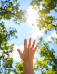 Hand reaching up toward bright sky, lush trees