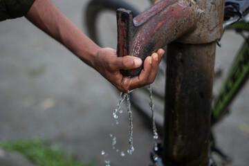 A persons hand catches water from an old hand pump, with a bicycle in the background