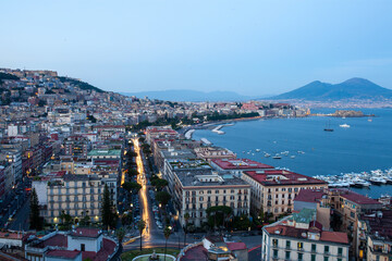 Obraz premium Naples waterfront cityscape depicting urban density coastal panorama usable in travel promo or architectural lighting design, illustrating sunset ambiance over Mediterranean harbour in low light